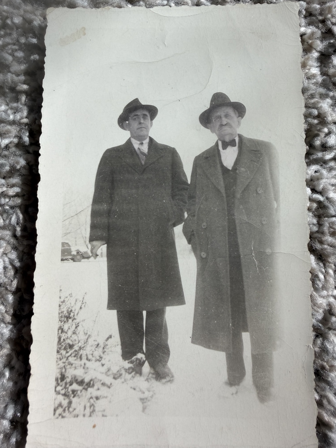Two men in overcoats and hats standing outside in snow.
