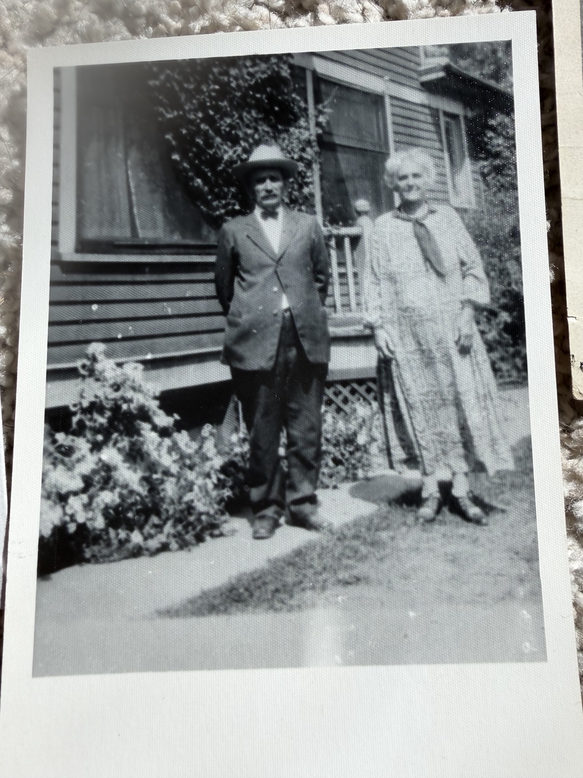A man and a woman standing beside the porch of a wooden house.