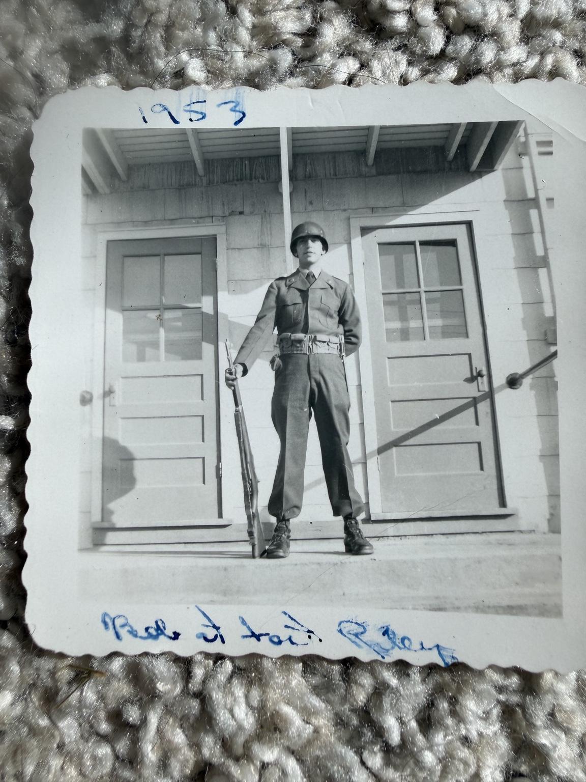 A uniformed man holding a rifle while standing on steps outside a building.