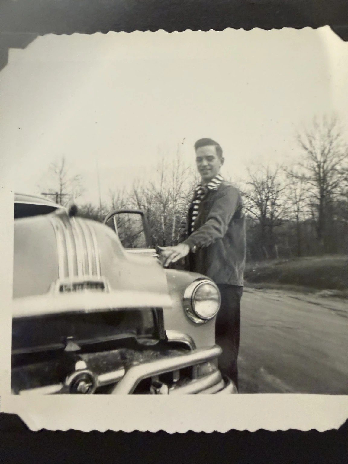 Bob, identified in the family collection, beside a car. Exact place and date are unconfirmed; no vehicle year, model or ownership is assigned.