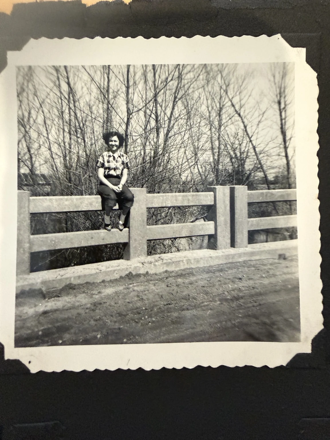 Bridget, identified in the family collection, seated on a bridge railing. The bridge location and exact date are unconfirmed.