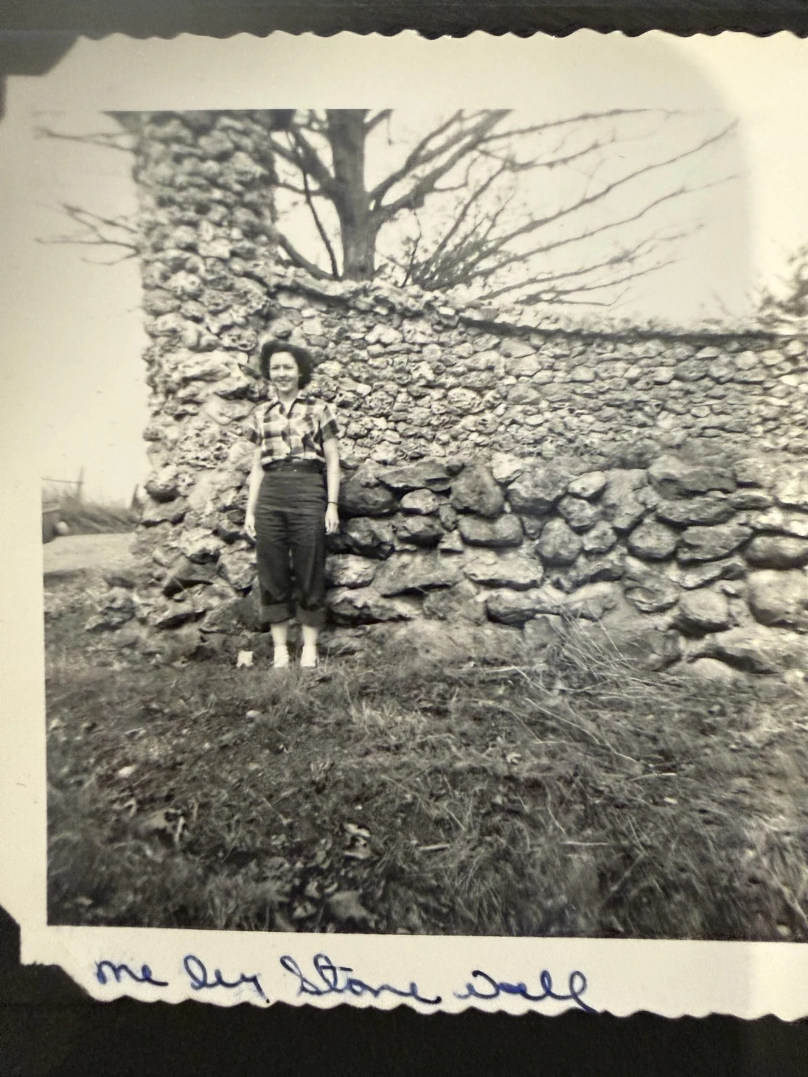 “me by stone wall” (original caption). The family collection identifies the person as Bridget. Exact place and date are unconfirmed.