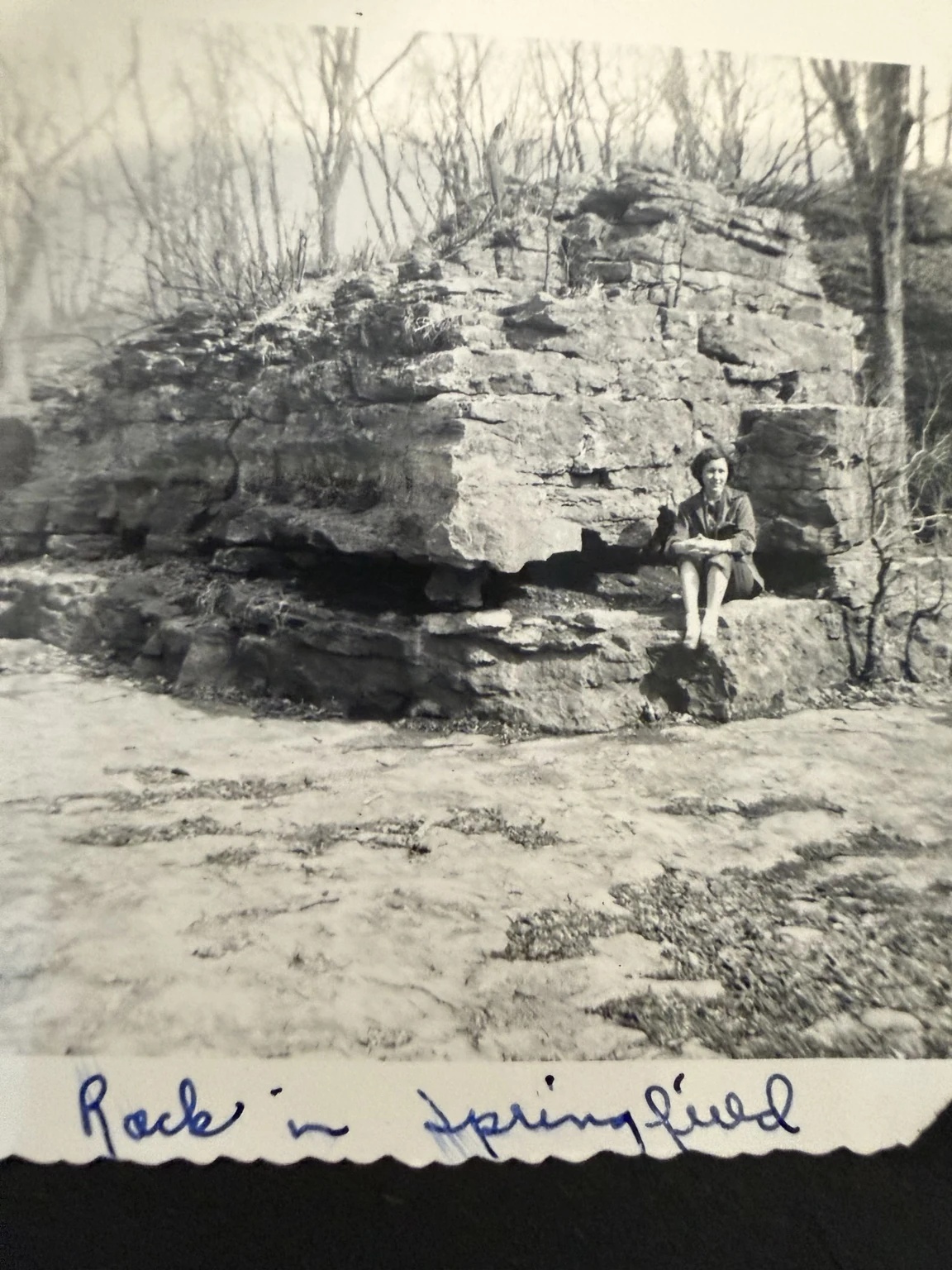 “Rock in Springfield” (original caption). A person seated beside the rock formation. Exact site, individual identification and date are unconfirmed here.