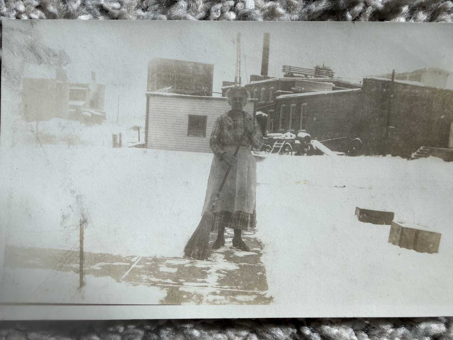 A woman standing in a snow-covered yard with outbuildings behind her.