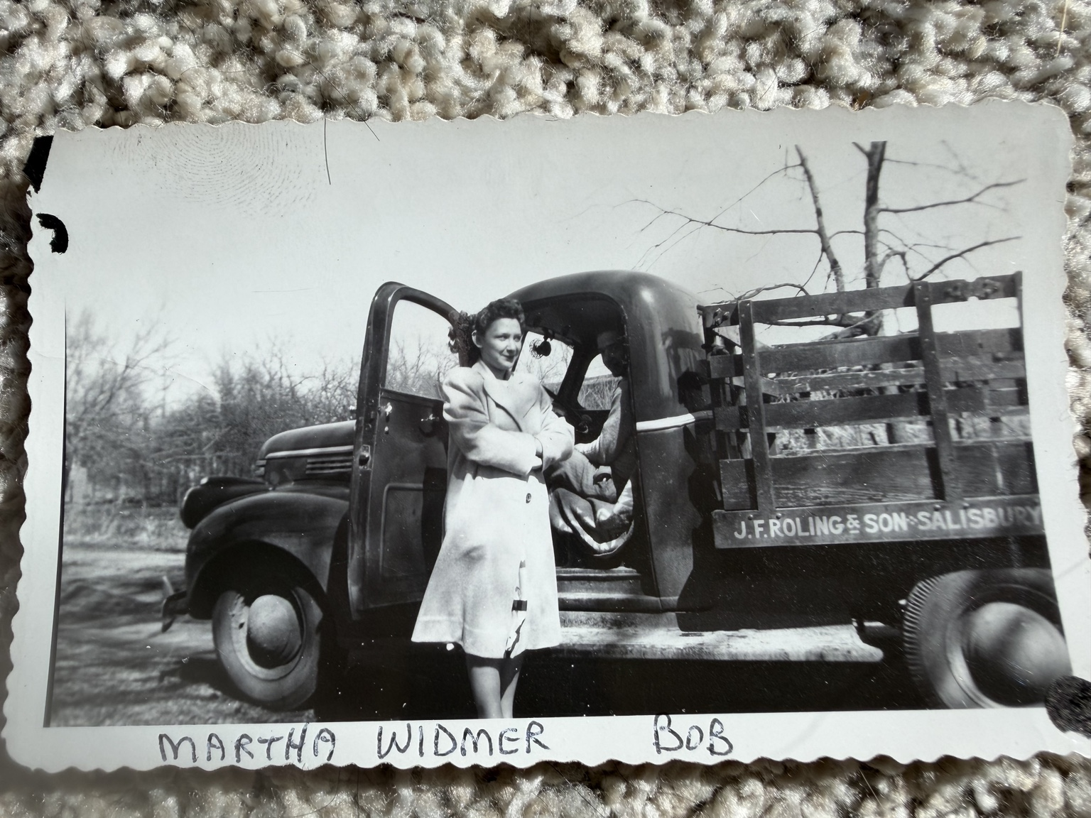 A woman beside the open cab of a truck, with a second person inside; the truck carries J.F. Roling & Son lettering.