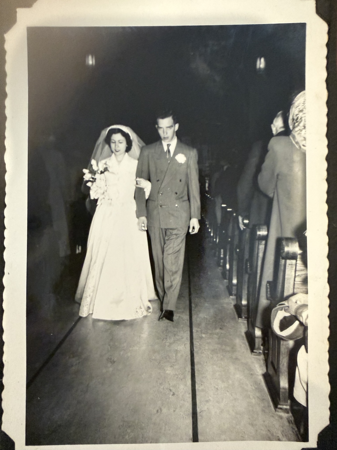 Bride and groom walking through a church aisle, seen at closer range.