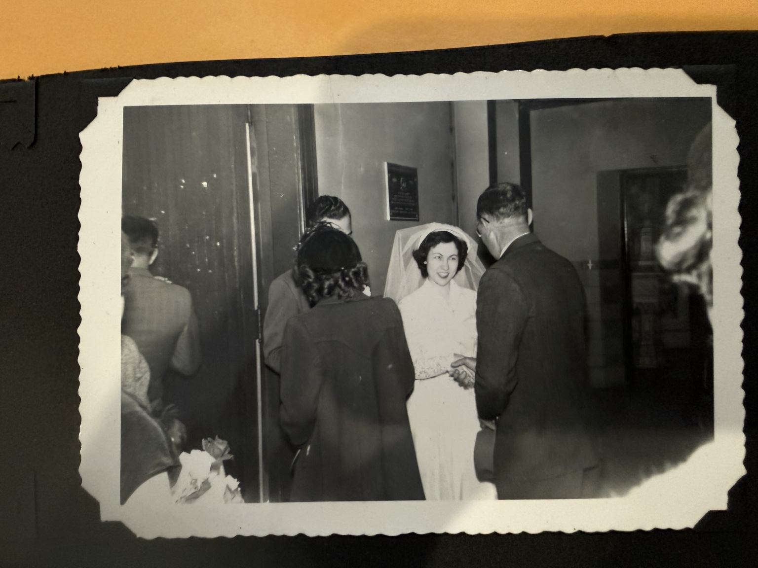 The bride greeting people in a doorway, partly surrounded by figures seen from behind.