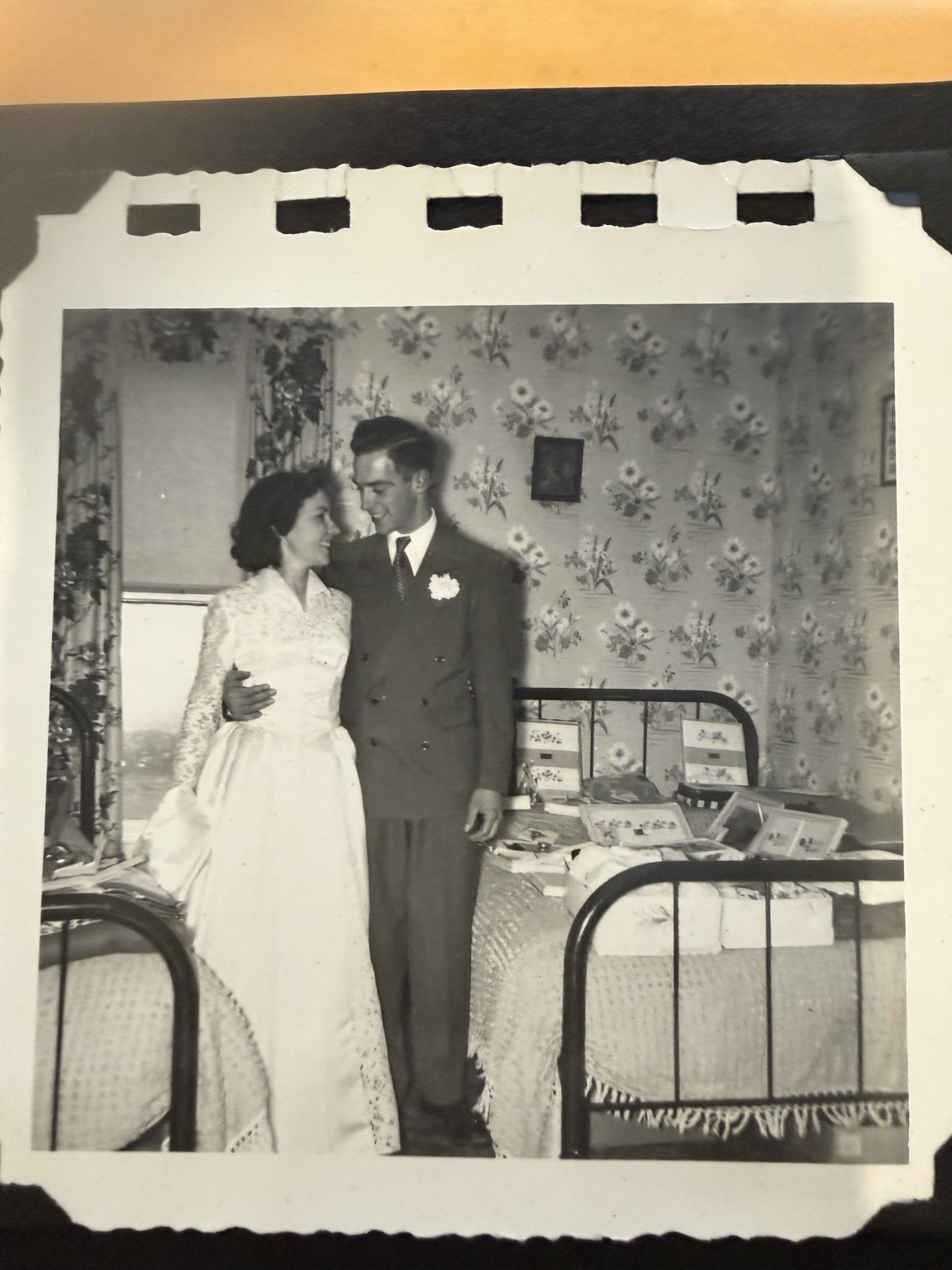 Bride and groom looking toward one another beside a display of boxed gifts.