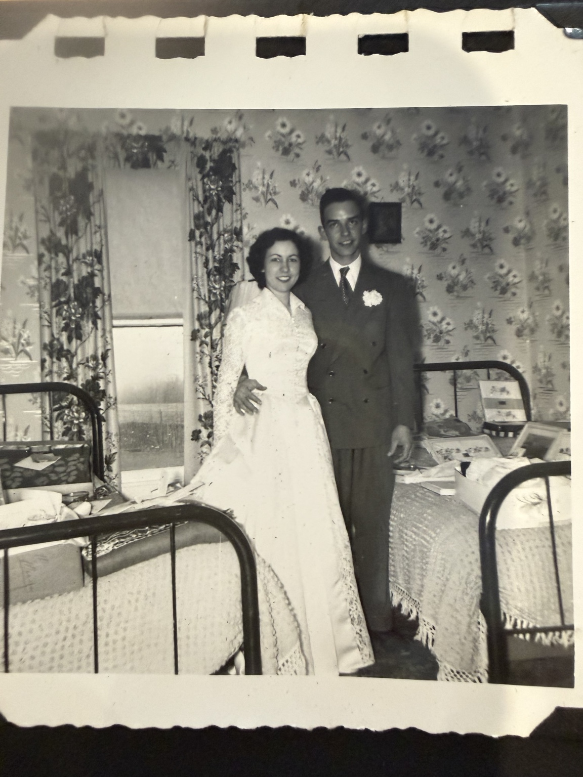 Bride and groom posed toward the camera beside a display of boxed gifts.