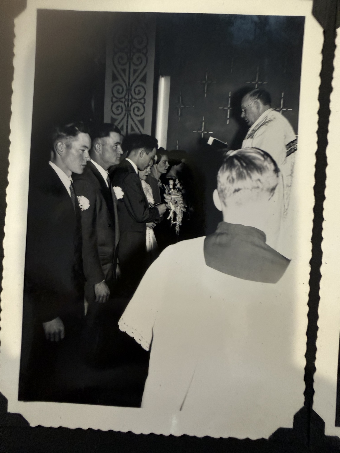 Wedding-party members facing a clergyman during the ceremony, with a robed attendant in the foreground.