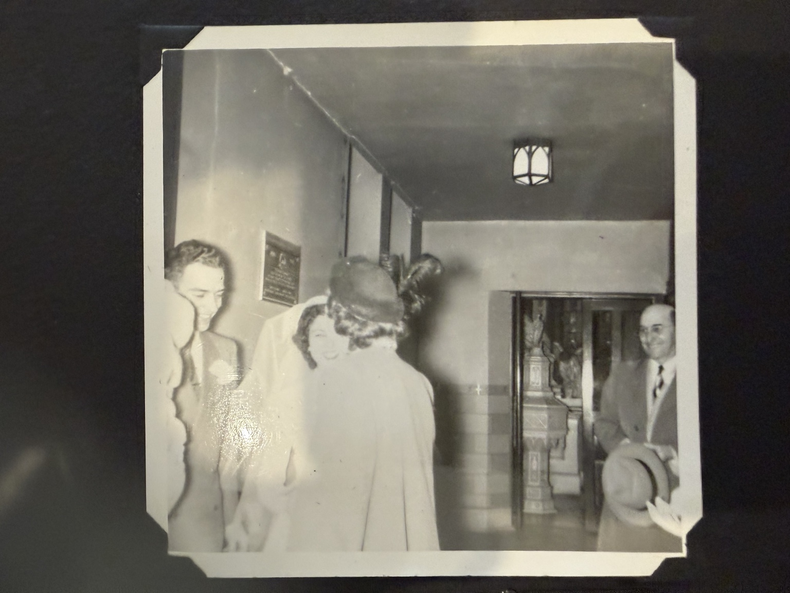 A group gathered in a hallway, with a woman seen from behind in the foreground.
