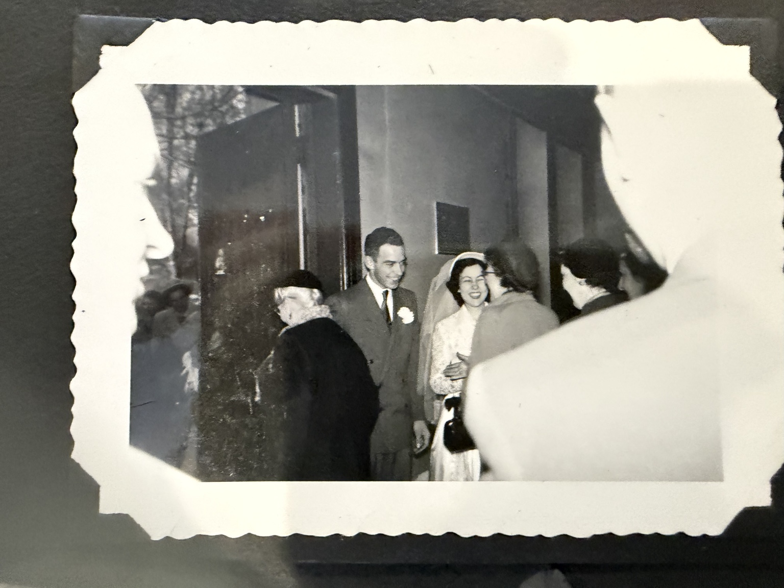 Bride and groom among a group greeting one another by a doorway.