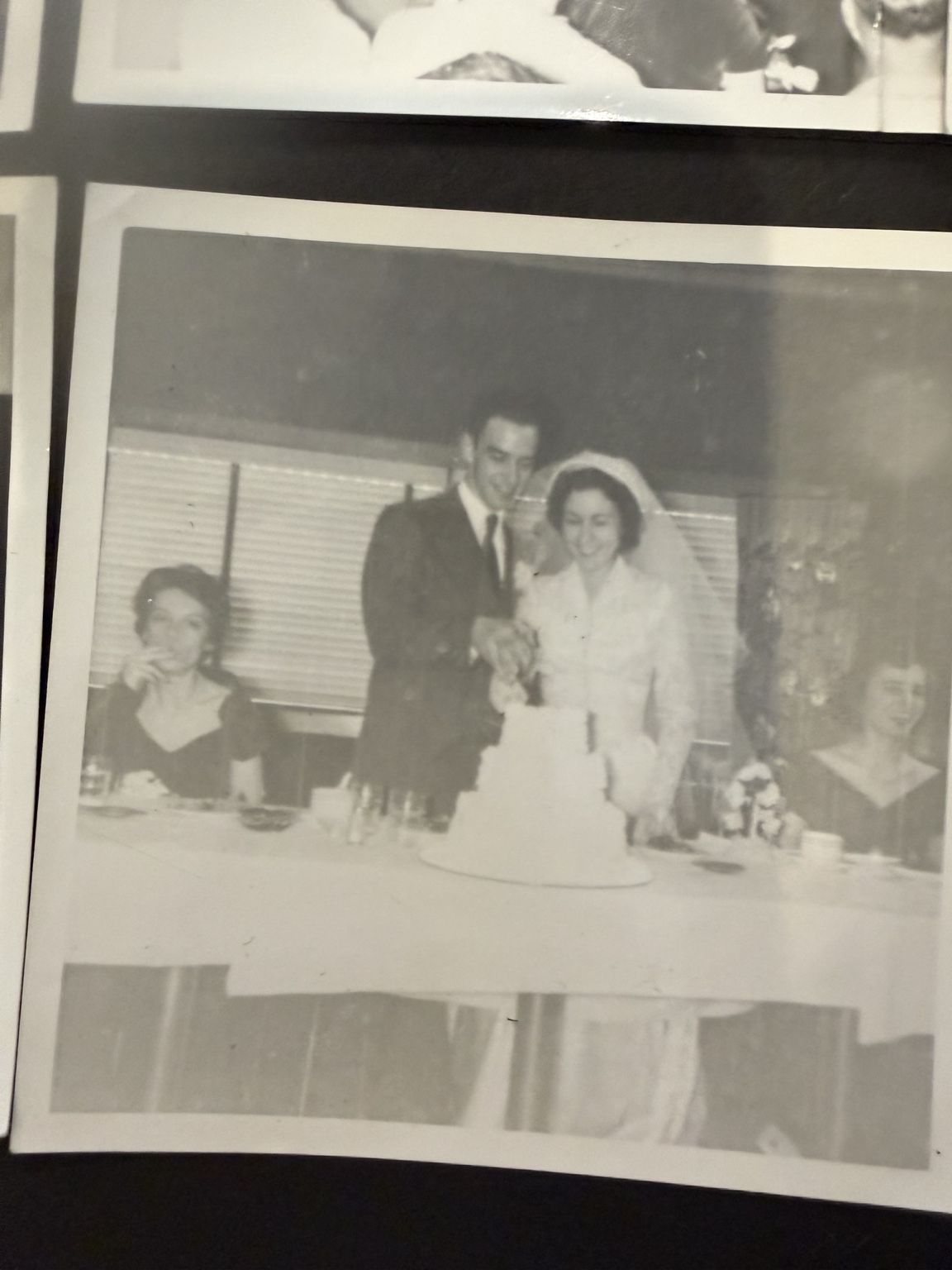Bride and groom standing together behind a tiered cake at a table, with seated people to either side.