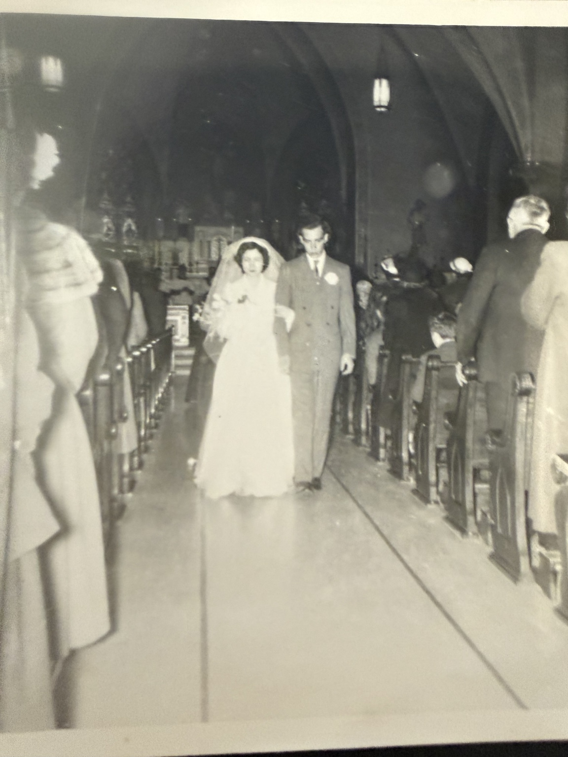 Bride and groom walking through the church aisle, seen from farther away with guests beside the pews.