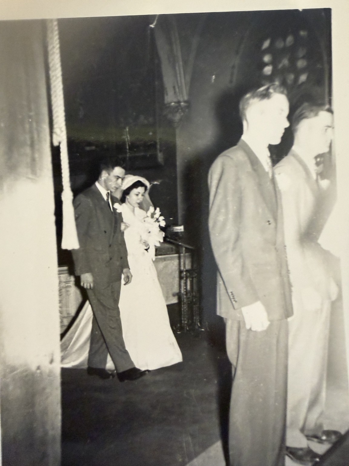 Wedding-party members walking through the church, with two people in the foreground and the bridal couple behind.